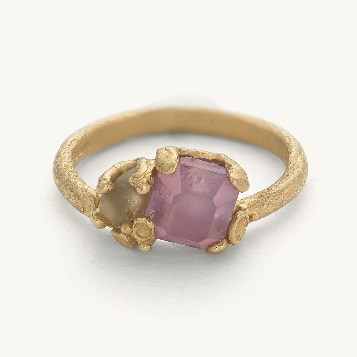 Handcrafted gold ring with a semi-cut pink sapphire and a raw sapphire with barnacle details. Designed by Ruth Tomlinson and handmade in London.