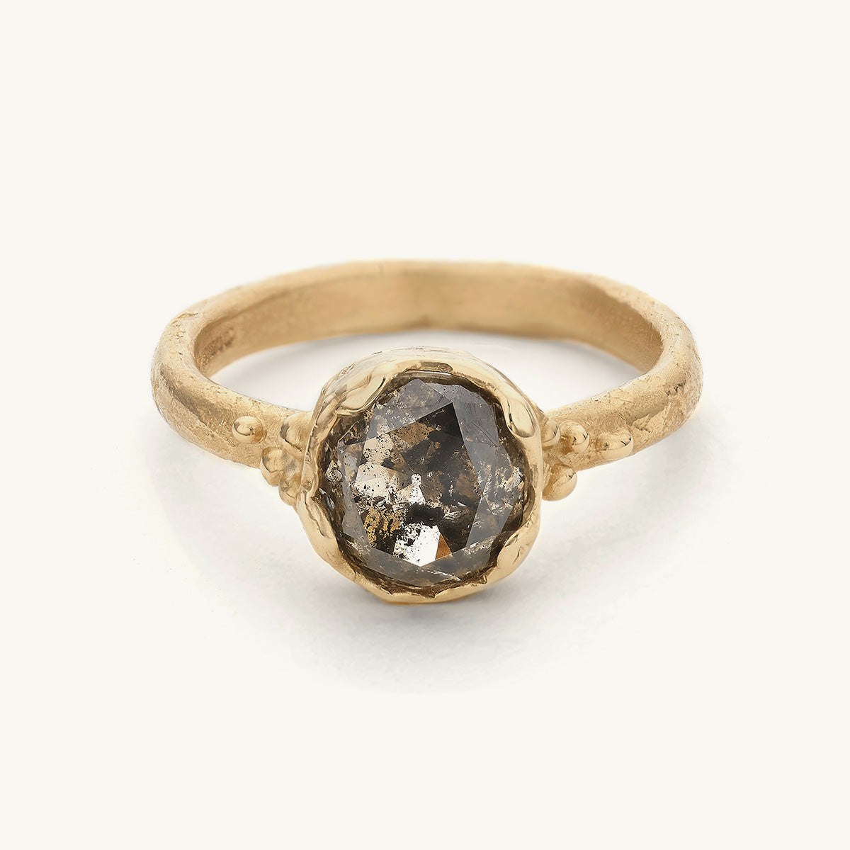 Alternative Solitaire diamond engagement ring designed by Ruth Tomlinson. A diamond flecked with inclusions creating a unique pattern, set in an organic bezel style setting with golden granule details. 