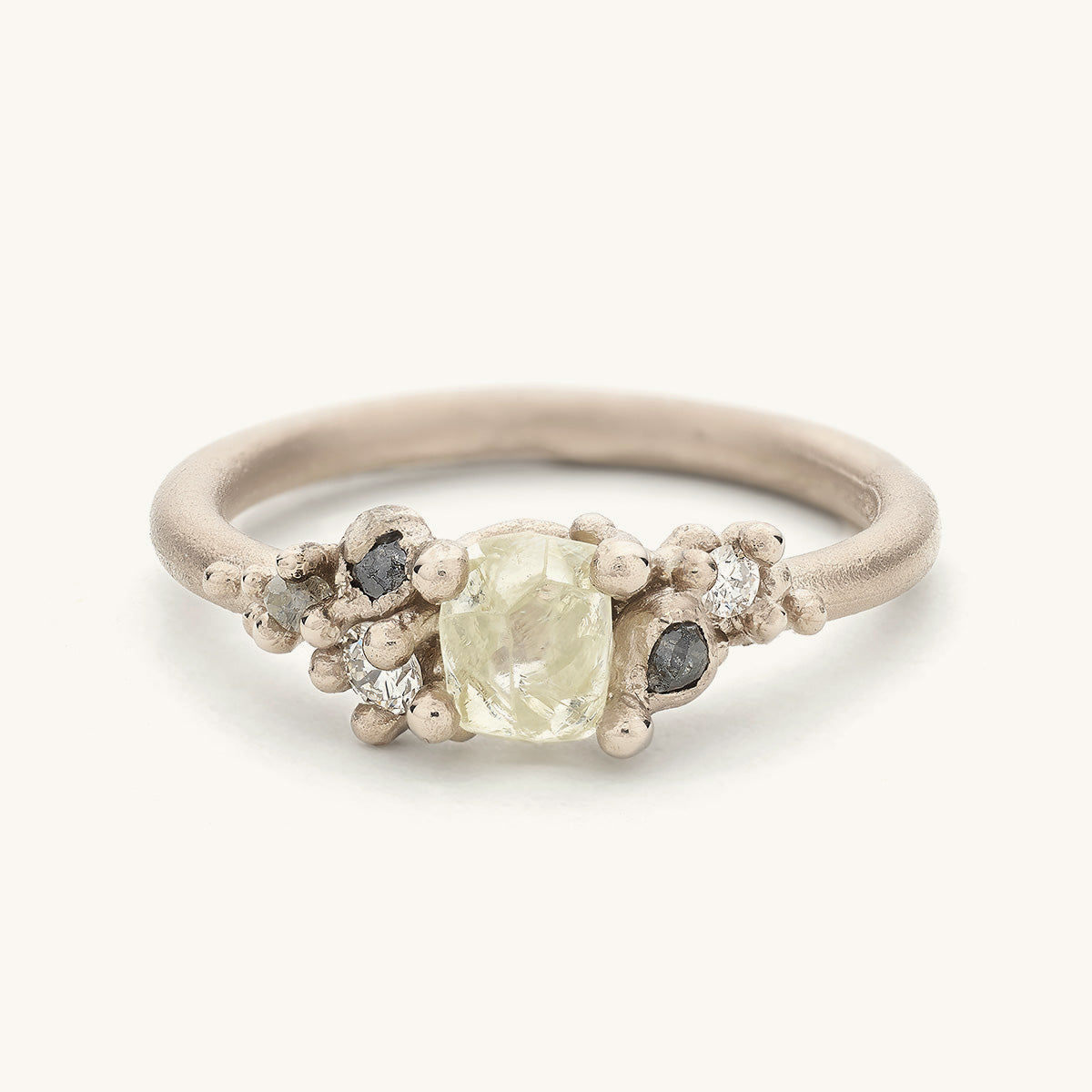 Raw diamond engagement ring by Ruth Tomlinson. The central raw diamond is framed on each side by asymmetric clusters of mixed cut diamonds and white gold details. 