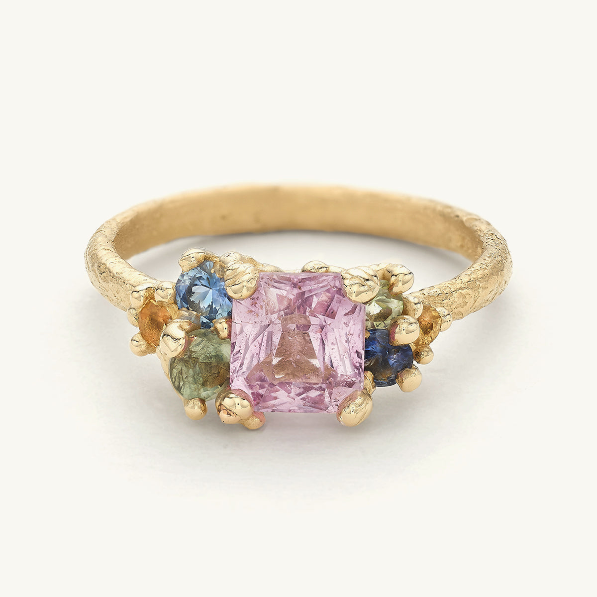 one-of-a-kind alternative engagement ring with a pale pink sapphire framed by colourful clusters of sapphires. Handcrafted in London with recycled gold and responsibly sourced gemstones.