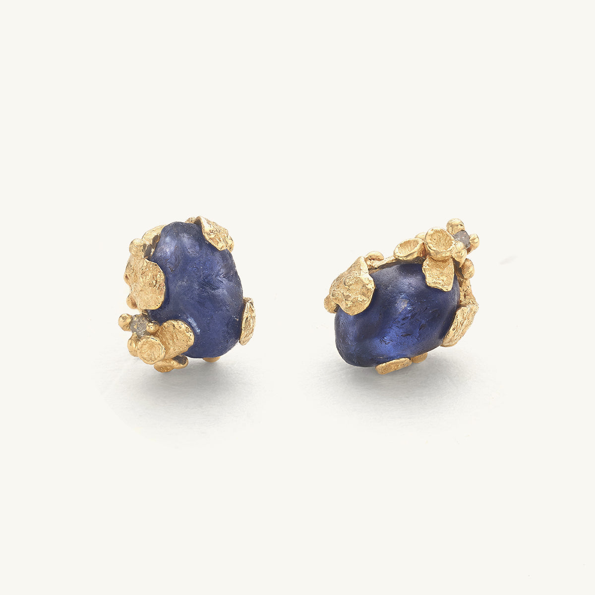 Pair of raw blue sapphire studs with organic golden details on a white background