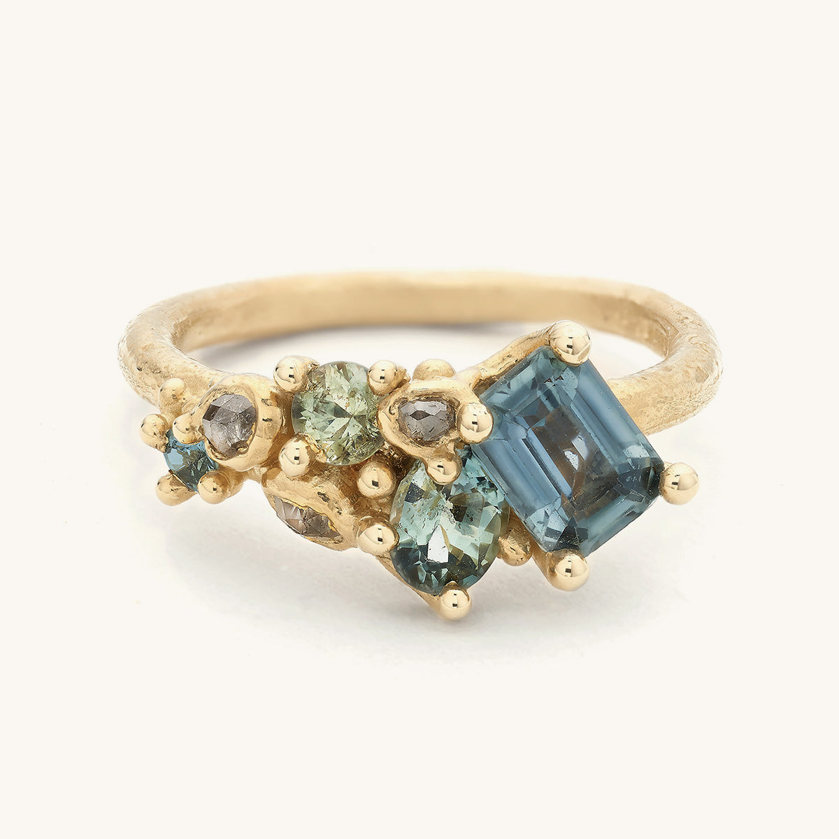 Handcrafted engagement ring by Ruth Tomlinson featuring an asymmetric tapering cluster of sapphires and grey diamonds amongst organic golden details. 